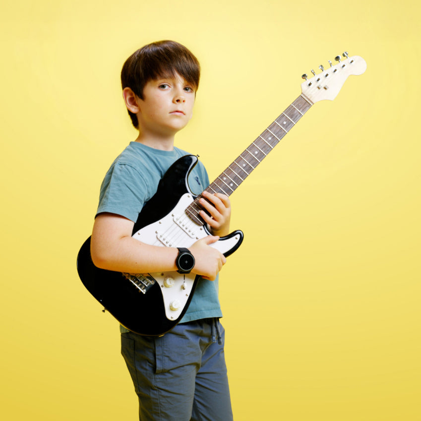 Bambino che tiene una chitarra elettrica bianca e nera e indossa un dispositivo da polso nero