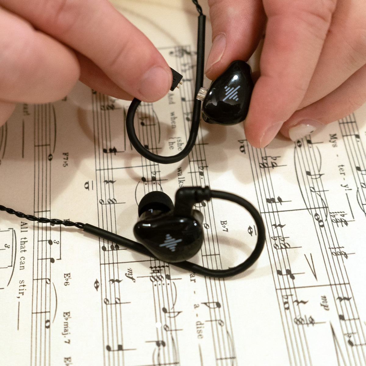 Black in-ear monitors and cable resting on sheet music