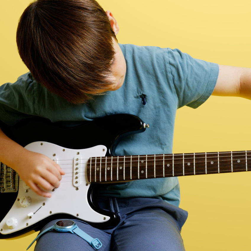 Child playing electric guitar with a blue Spark practice companion on their leg