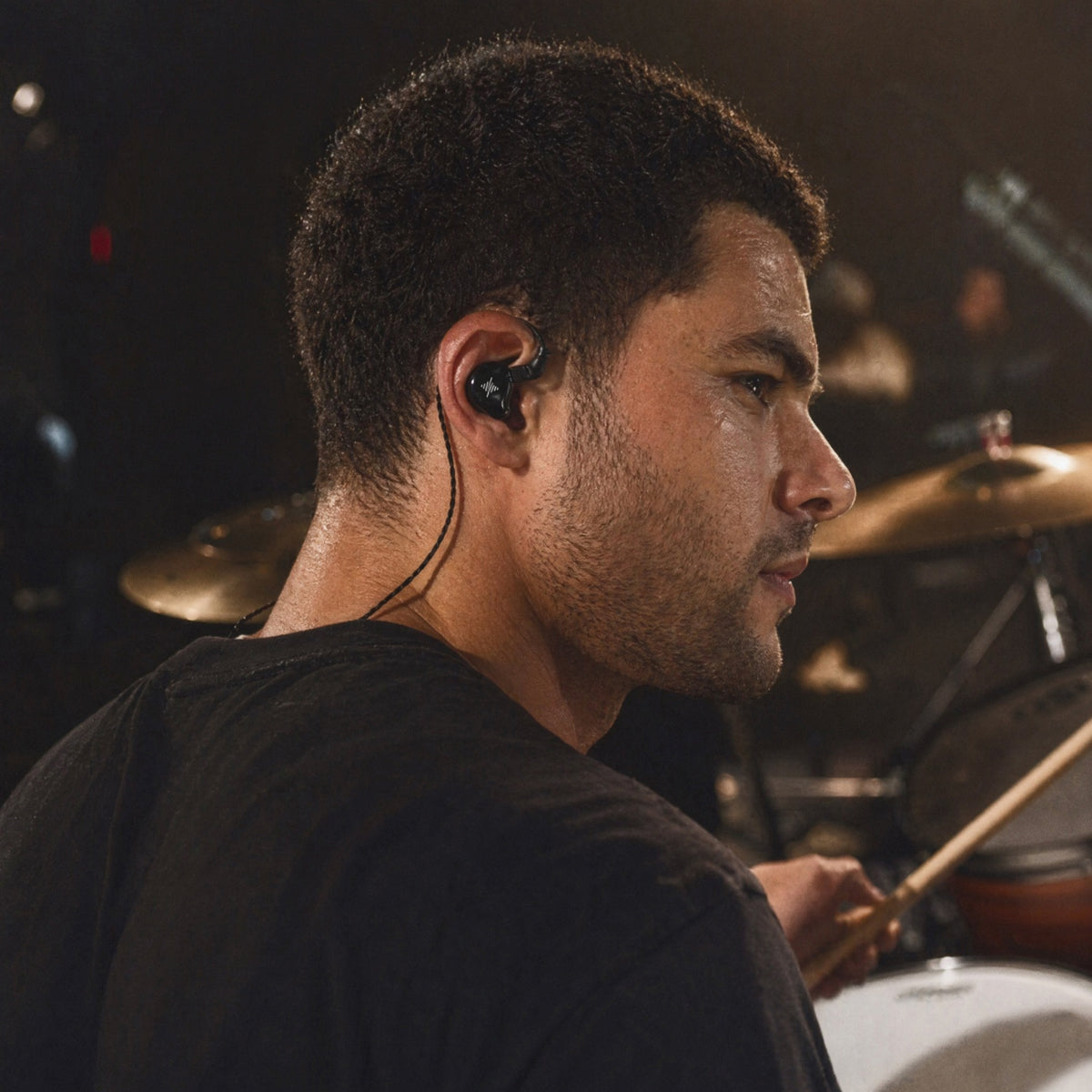 Drummer wearing a black in-ear monitor while performing on stage