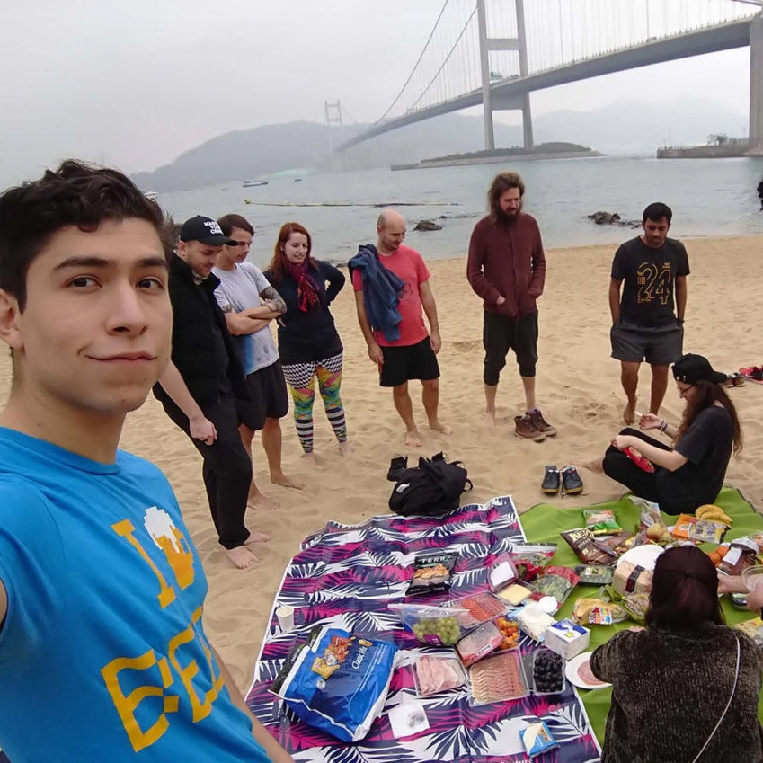 Group picnic on a beach beneath a suspension bridge