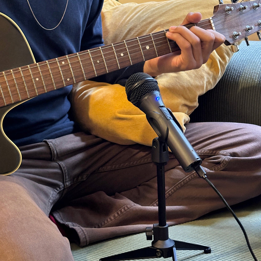 Person playing an acoustic guitar beside a microphone on a stand