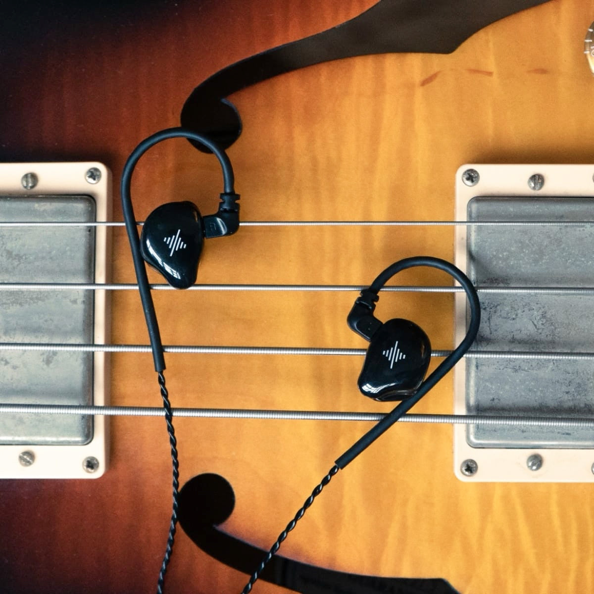 Black wired in-ear monitors resting on the strings of an electric guitar