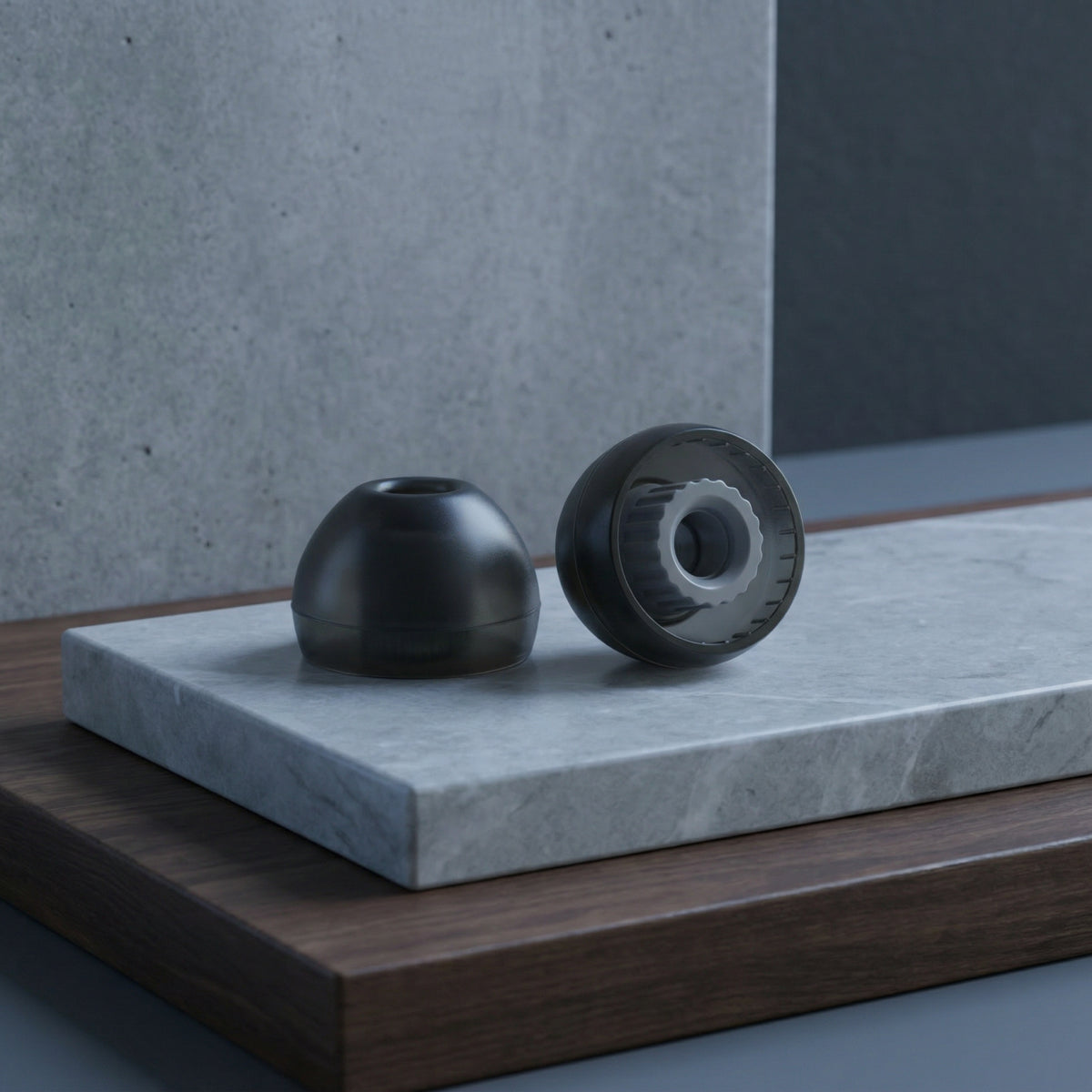 Two black Liquid Pro ear tips displayed on a gray stone block