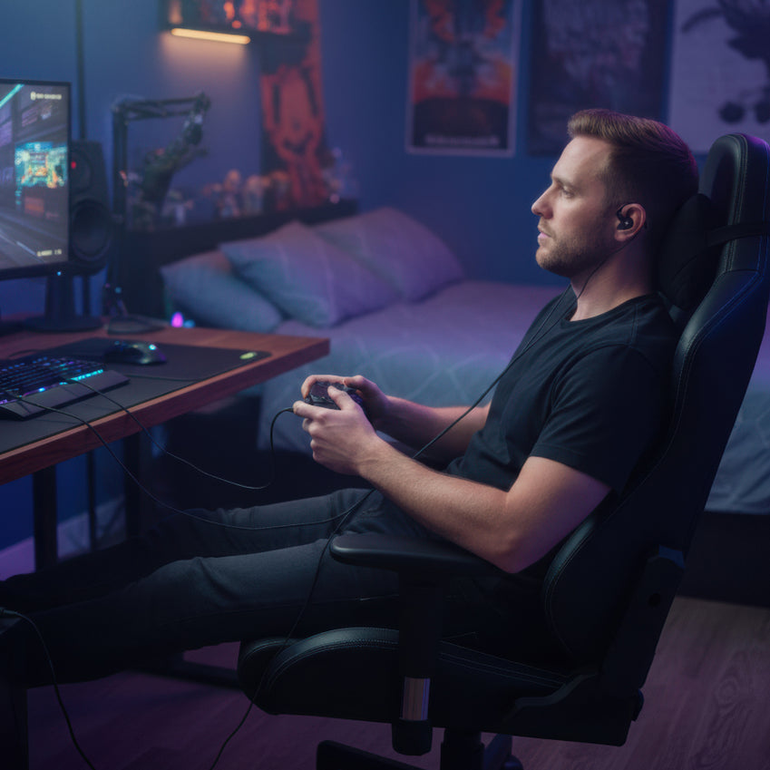 Man wearing an in-ear monitor while holding a game controller in a gaming chair