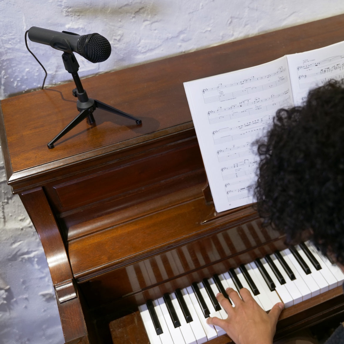Black microphone on a tripod beside a piano as a person plays the keys