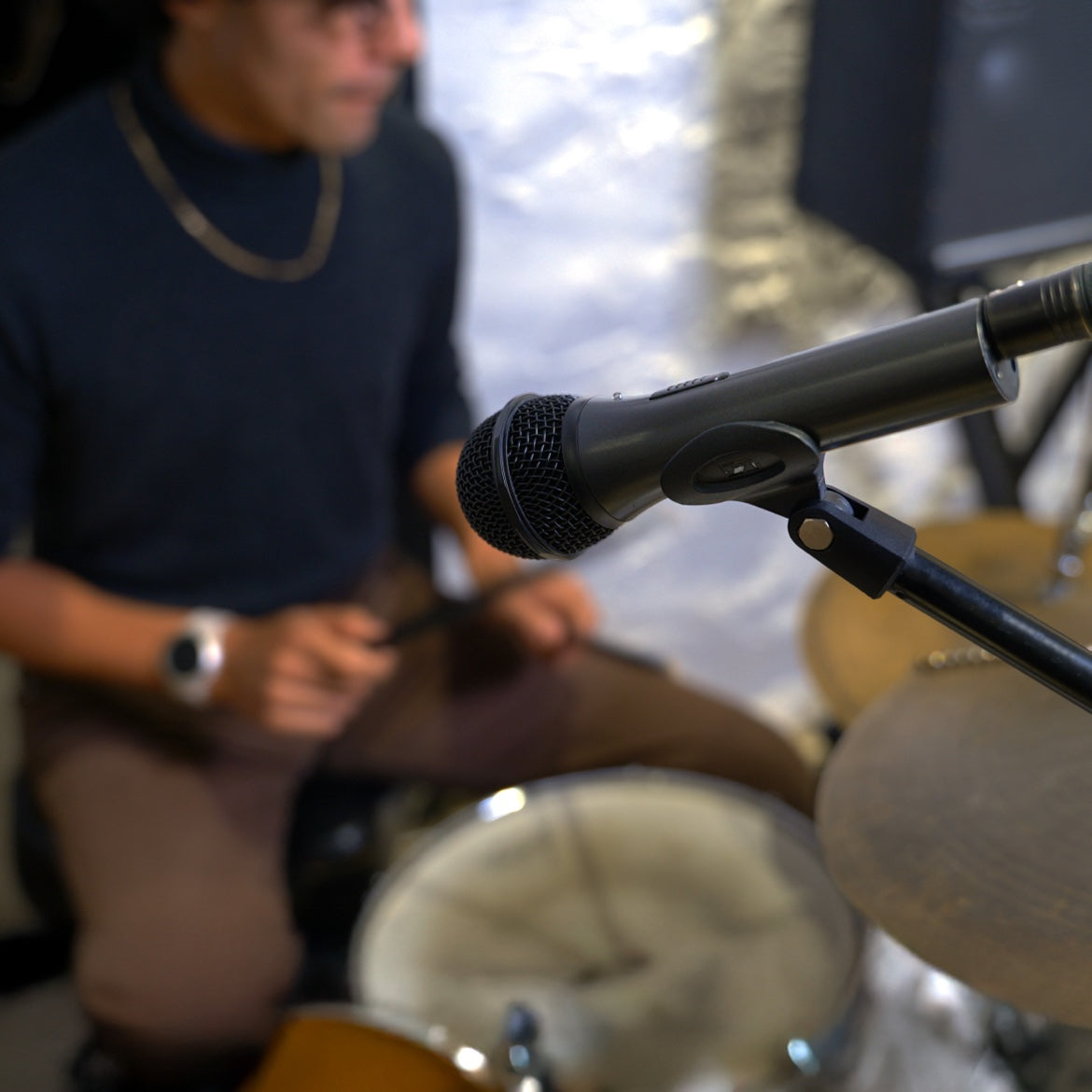 Black microphone on a stand in front of a seated drummer