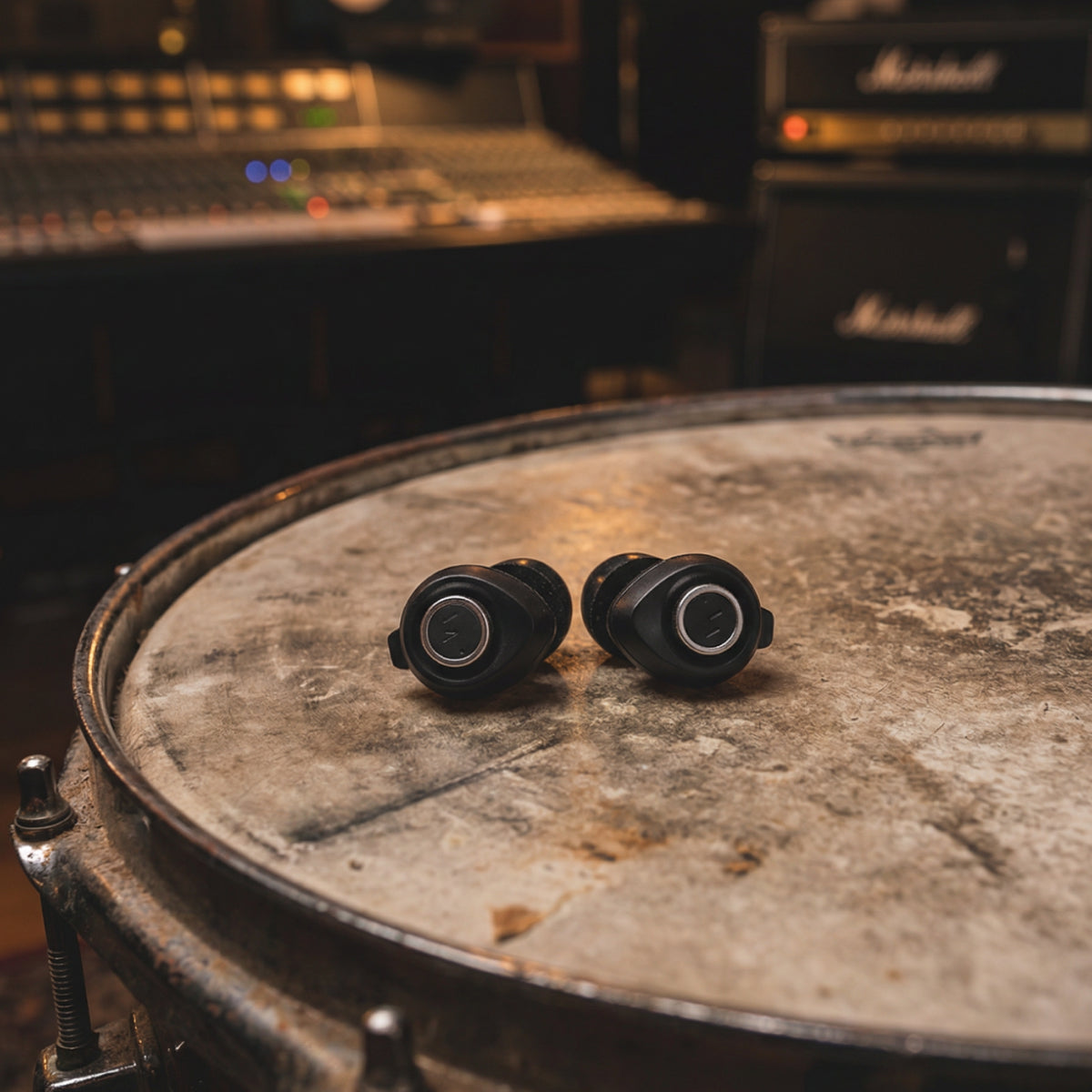 Two black Minuendo earplugs on a drum with studio equipment in the background