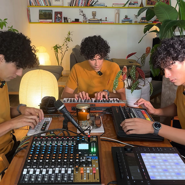 Three musicians play electronic instruments together; a black wearable is visible on one person's wrist