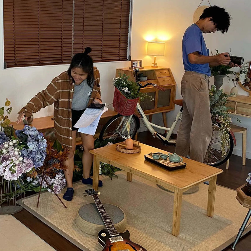 Two people among flowers and a bicycle indoors