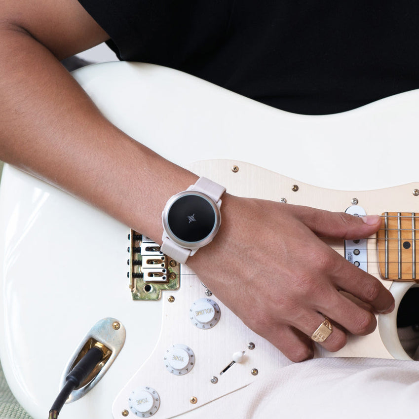 Person playing a white electric guitar while wearing a round wrist device
