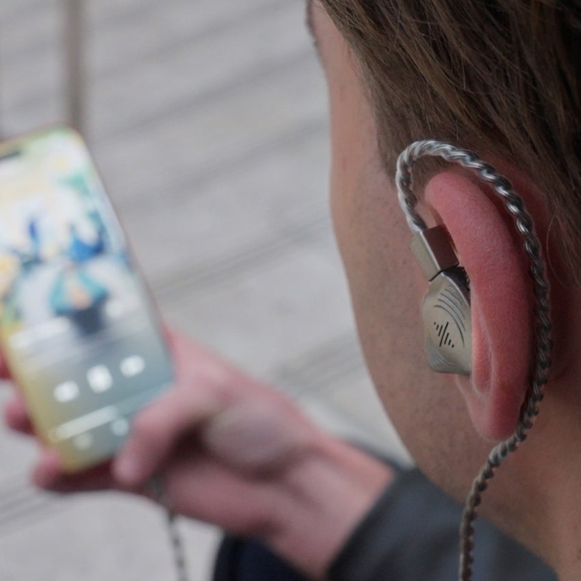Person wearing a silver in-ear monitor while holding a smartphone