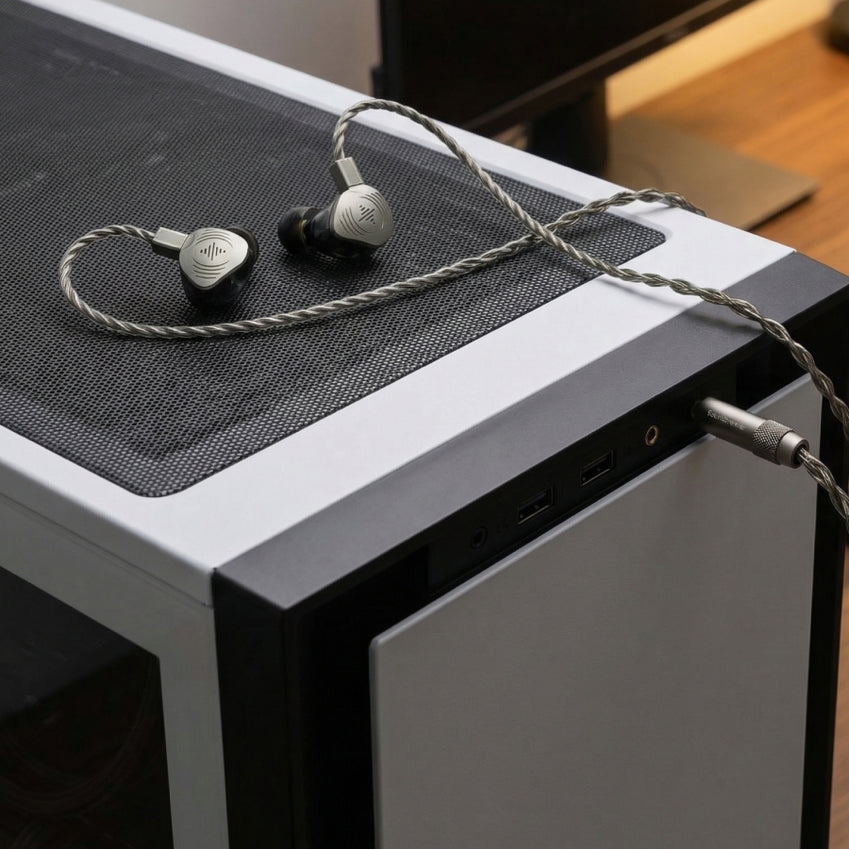 Silver wired in-ear monitors resting on a desktop computer