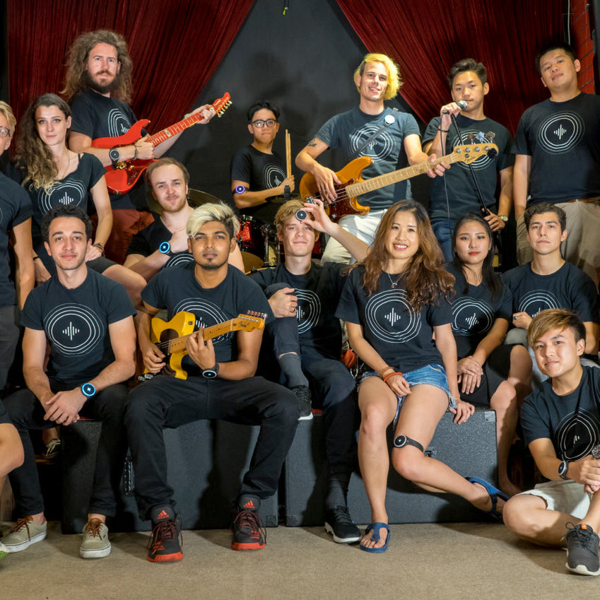 Group of people wearing Soundbrenner shirts pose with guitars and basses