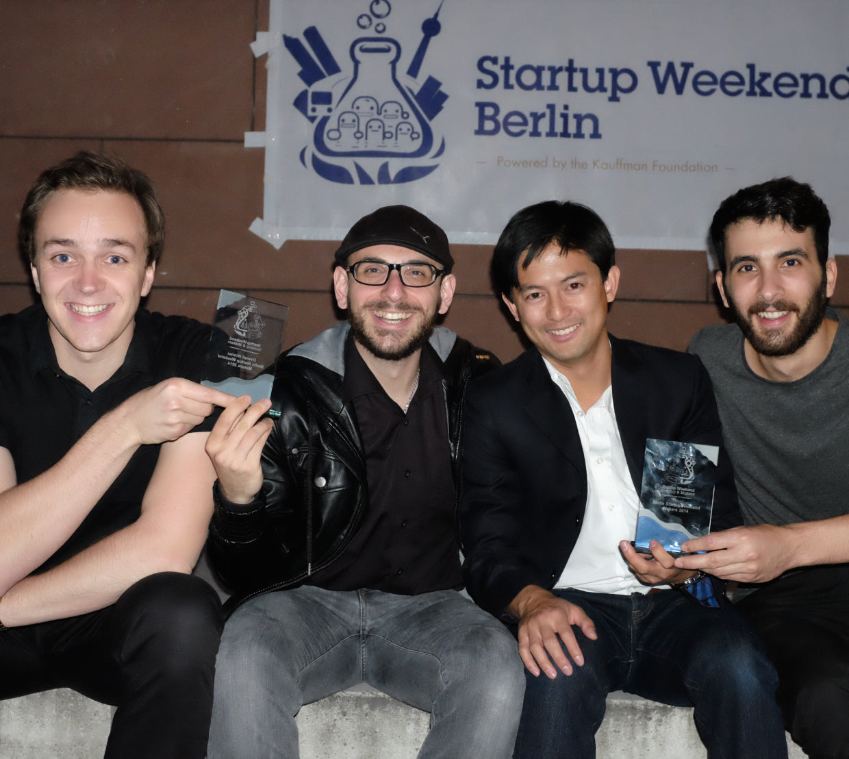 Four men sitting together beneath a Startup Weekend Berlin sign