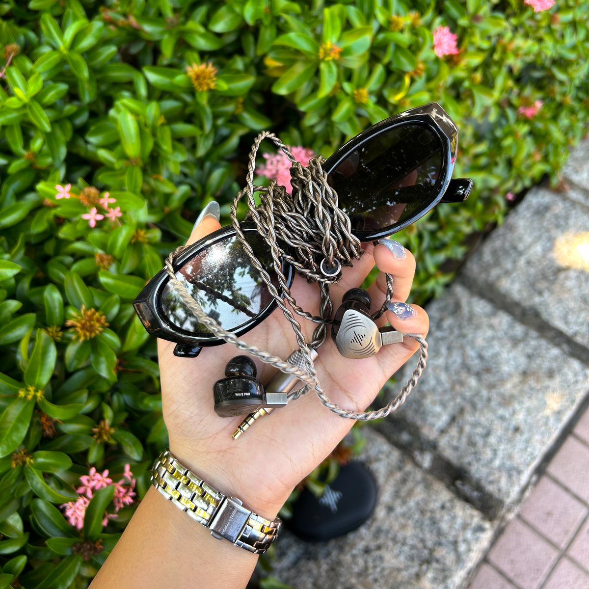 Wave Pro 2 earphones and sunglasses held outdoors