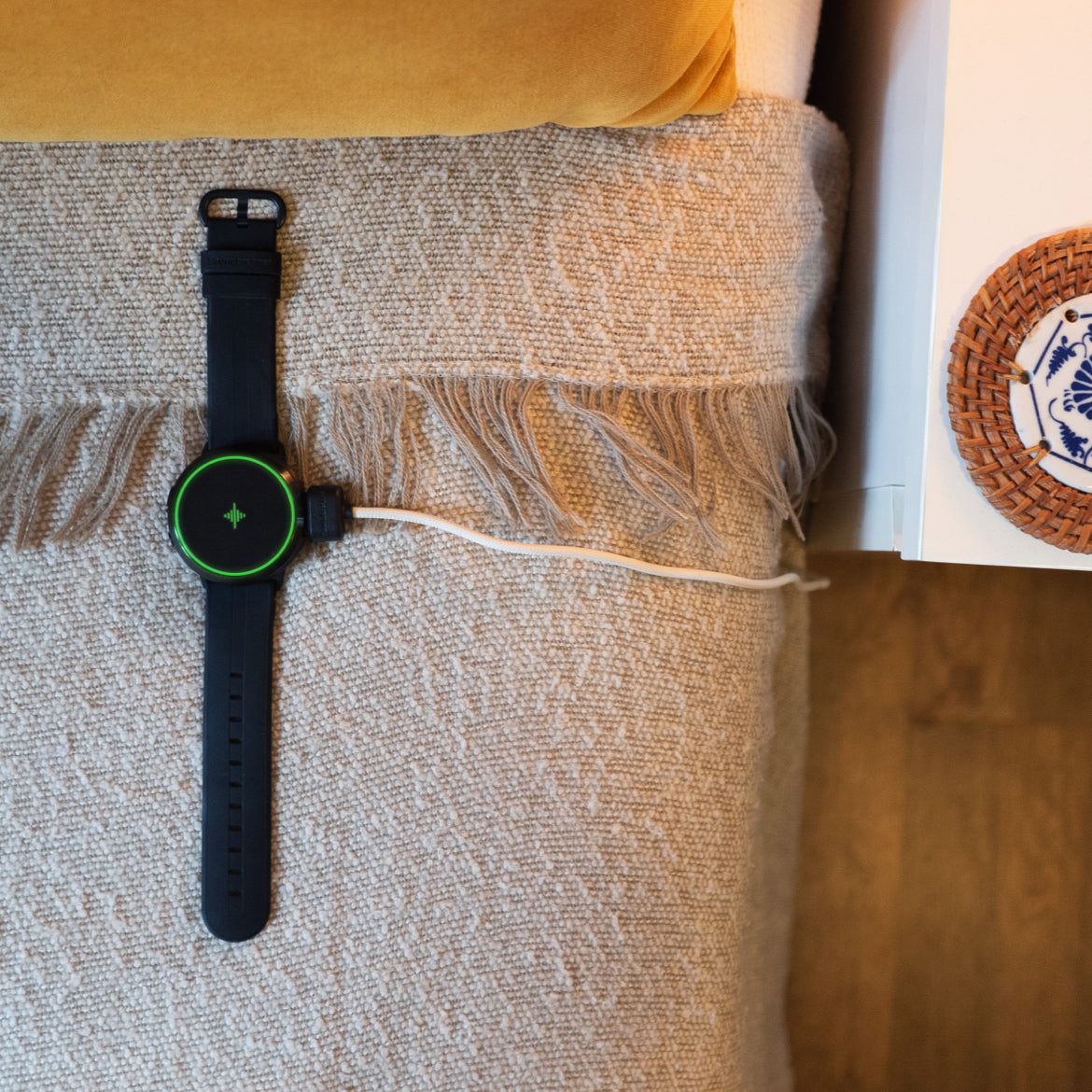 Black wearable device and white charging cable resting on a woven blanket