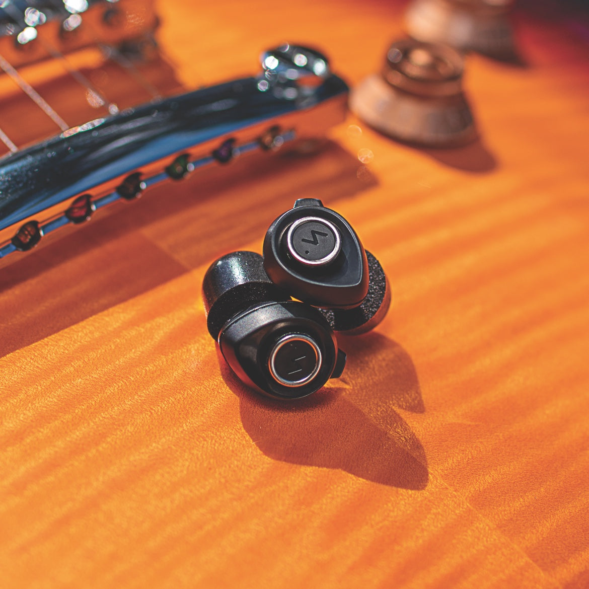 Black Minuendo earplugs resting on the body of a violin