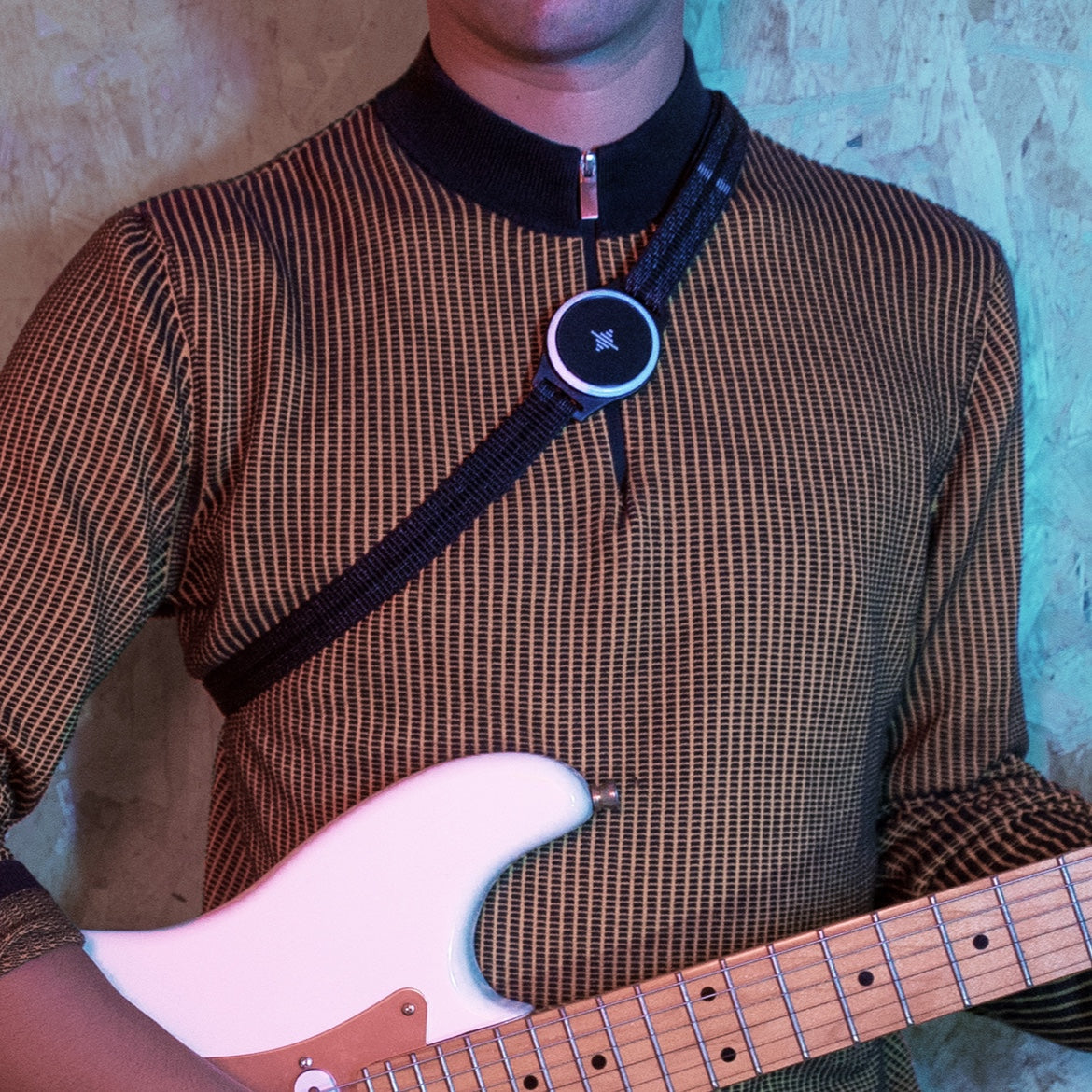 Músico con un metrónomo circular en una correa de pecho mientras sostiene una guitarra