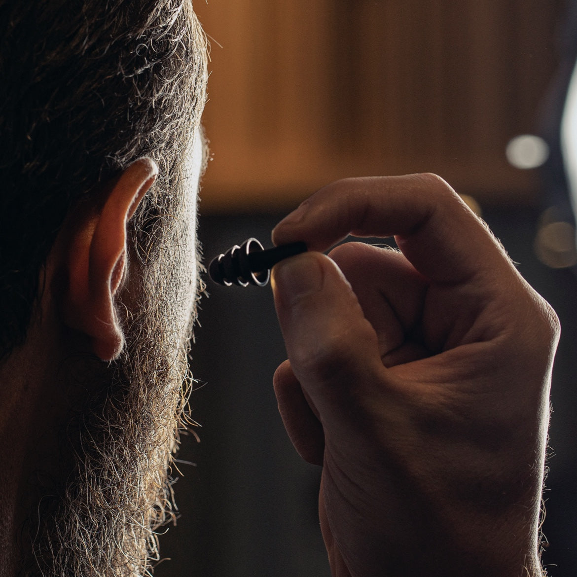 Person inserting a black earplug into one ear